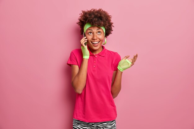 Cheerful positive curly haired teenage girl has telephone conversation