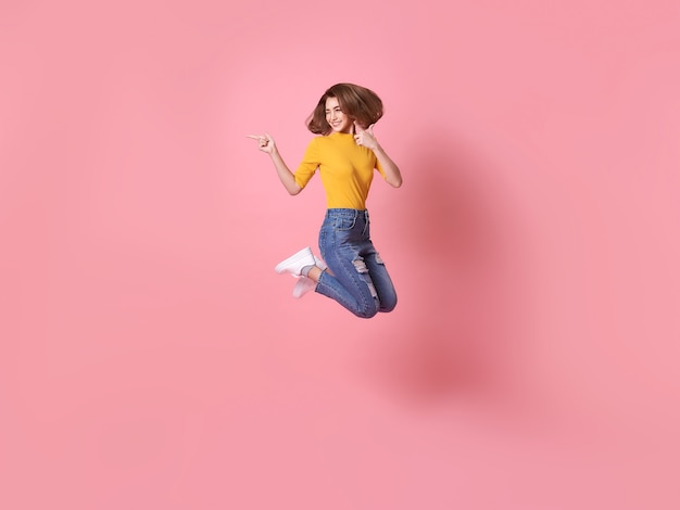 분홍색 배경에 고립 된 공간을 복사를 가리키는 제기 손으로 공중에 점프 명랑 긍정적 인 소녀.