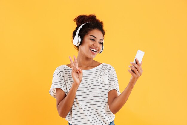 Жизнерадостная положительная молодая женщина в наушниках используя изолированный телефон