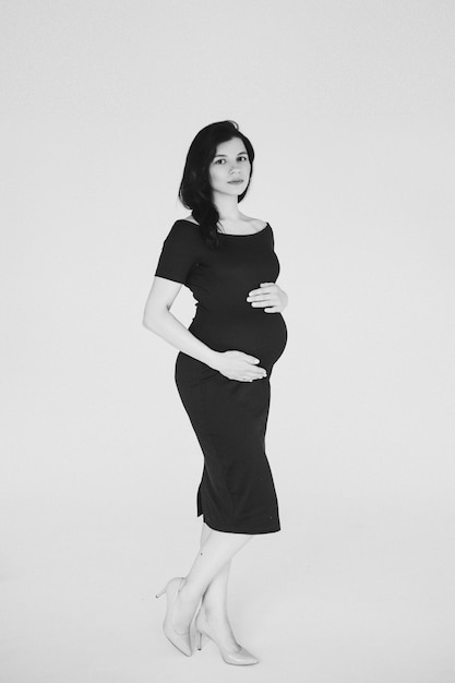 Веселая беременная кавказская женщина ждет своего ребенка и трогает ее животик, черно-белое изображение на белом фоне