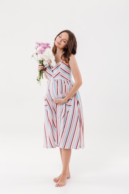 Cheerful pregnant woman holding flowers with eyes closed.