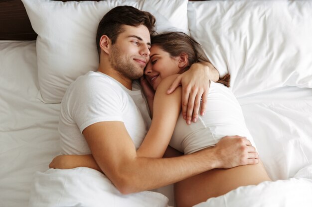 Веселая беременная женщина лежит в постели с мужем