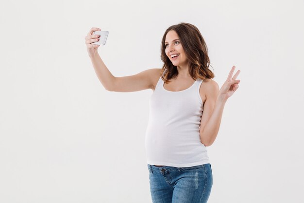 쾌활 한 임신 한 여자는 그녀의 아랫 배와 selfie를 확인