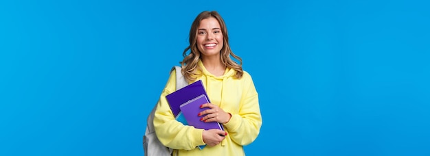 Free photo cheerful pretty blond girl smiling at camera carry backpack and notebooks papers for studying learni