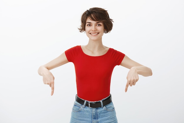 Cheerful pretty brunette woman pointing fingers down at announcement