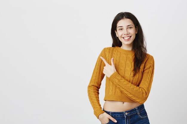 Cheerful pretty girl pointing upper left corner and smiling