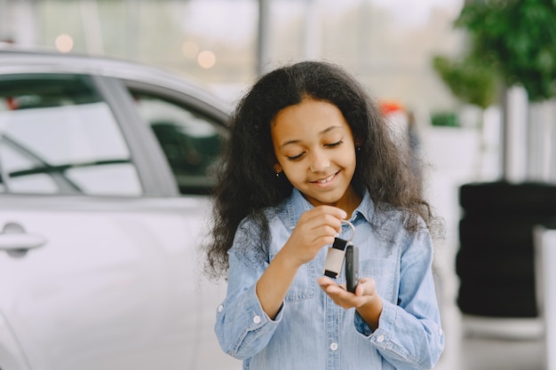 Cheerful, pretty little girl, holding car keys, showing it, smiling and posing.