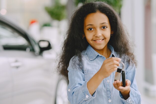 陽気でかわいい女の子が見て、車のキーを持って、それを見せて、笑顔でポーズをとっています。