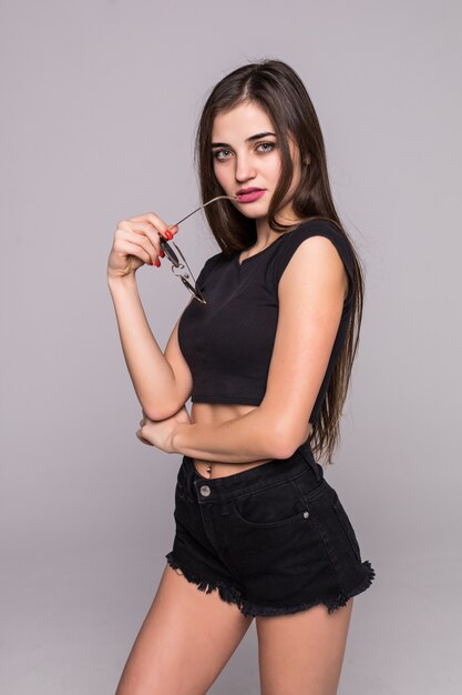 Cheerful pretty young woman holding sunglasses on a gray wall