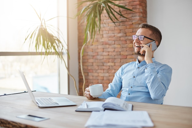 Cheerful professional adult caucasian finance manager in glasses and blue shirt sitting in company office