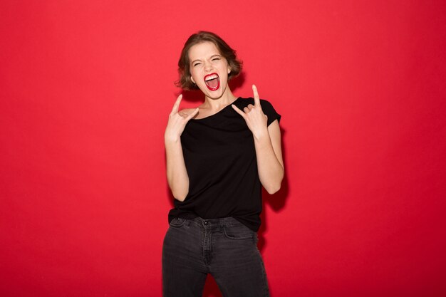 Cheerful punk woman screaming and showing rock gestures while looking