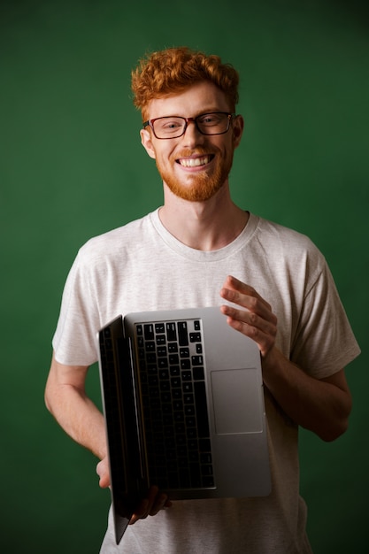 Cheerful readhead bearded man in glasses and white tshirt holding laptop in hands