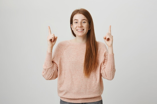 Cheerful redhead girl pointing fingers up , smiling