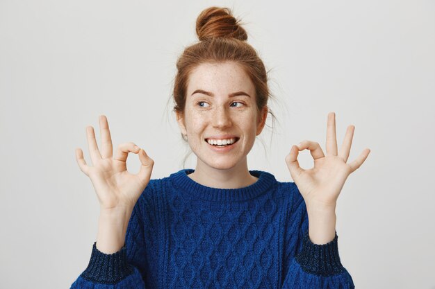 Cheerful redhead girl smiling, showing okay in approval, assure everything good