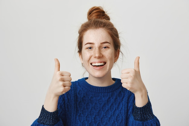 Free photo cheerful redhead girl smiling, showing thumbs-up in approval