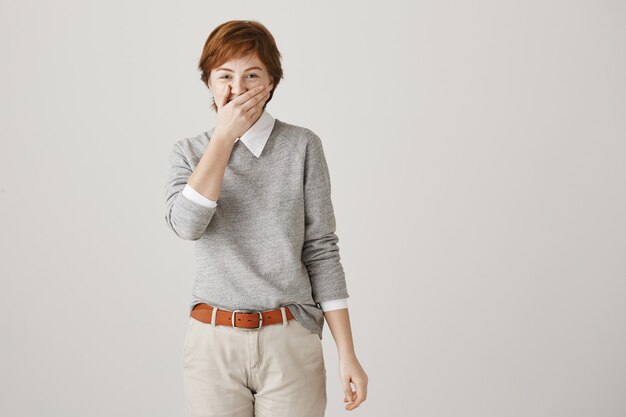 Cheerful redhead girl with short haircut posing against the white wall