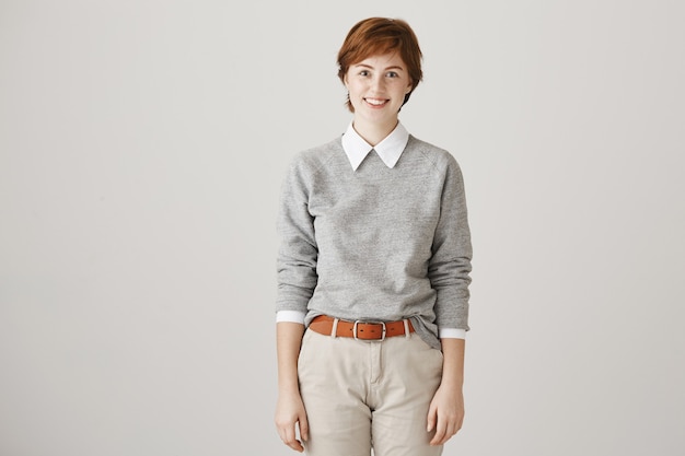 Cheerful redhead girl with short haircut posing against the white wall