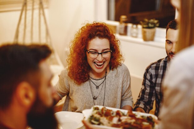 집에서 친구들과 저녁을 먹으면서 즐거운 시간을 보내는 쾌활한 빨간 머리 여성