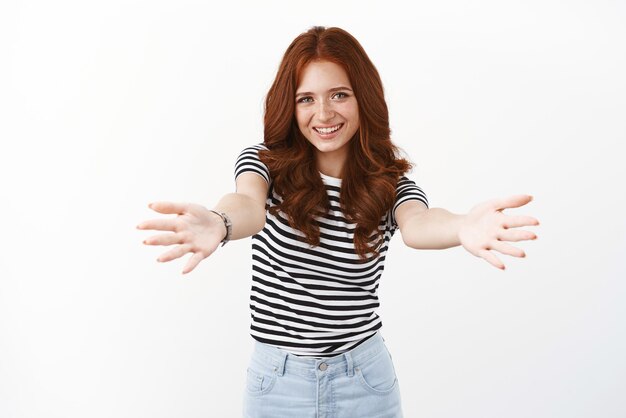Cheerful redhead woman in striped tshirt lean forward extend arms wanna hold or have something in her arms smiling joyfully hugging friend greeting with welcoming embraces white background