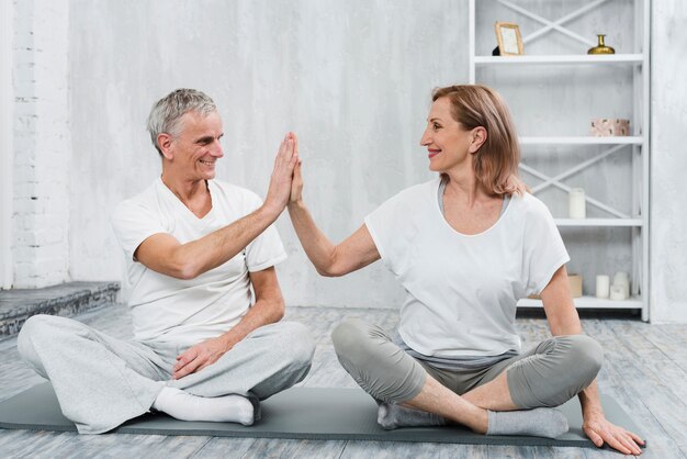 Cheerful senior couple giving high five while exercising together on mat