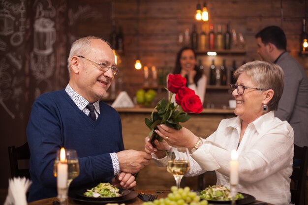 Cheerful senior couple happy about their date. Husband giving flower to his wife. Enjoying retirement.