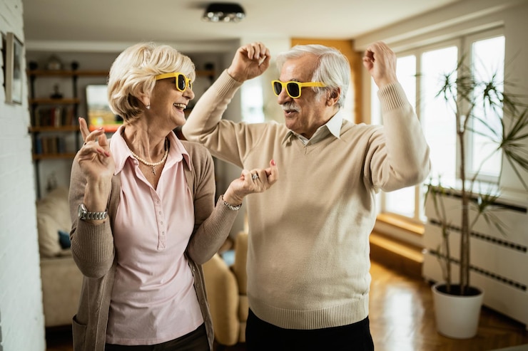 Free Photo cheerful senior couple with sunglasses dancing and having fun together at home