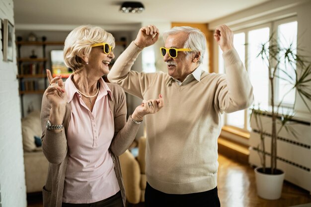 Cheerful senior couple with sunglasses dancing and having fun together at home