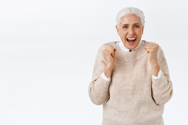 Cheerful senior lucky woman with grey hair in elegant outfit, old teacher finally got pension, cheering fist pump, clench arms and dancing as celebrating, smiling happily, triumphing achieve prize