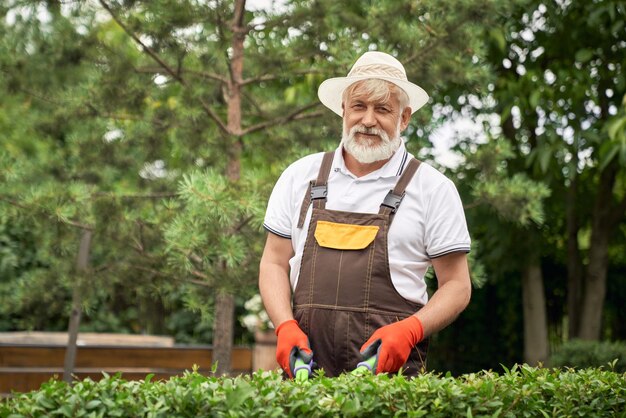 生い茂った茂みを切る陽気な年配の男性