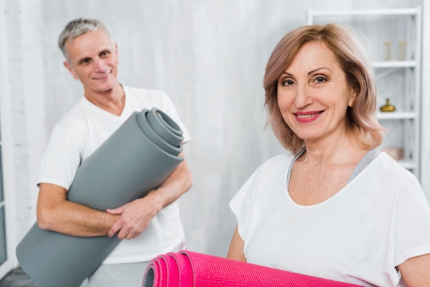 Cheerful senior man holding mat looking at his smiling wife