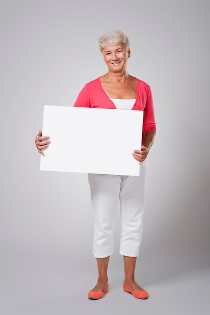 空白のホワイトボードを保持している陽気な年配の女性