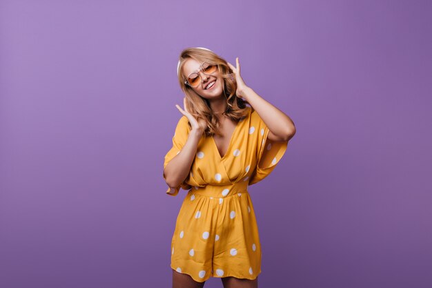 cheerful shapely girl posing with sincere smile on purple. gorgeous female model in stylish orange dress standing