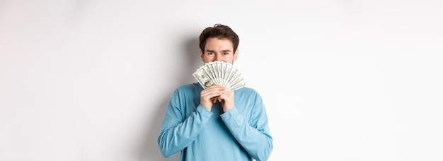 Free photo cheerful shopper holding money for shopping standing with dollars and smiling standing over white ba