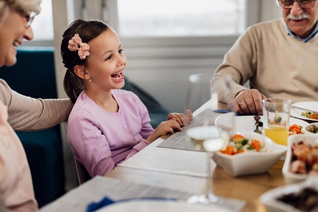 식탁에서 조부모와 함께 점심을 먹으면서 즐거운 시간을 보내는 쾌활한 작은 소녀
