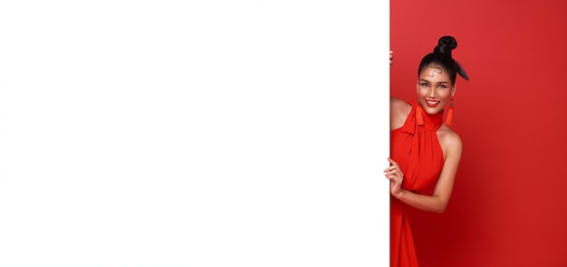 陽気な笑顔赤のカジュアルな服装の若いアジア女性が白い空白のバナーの後ろに立っています。
