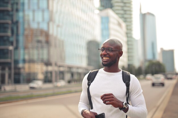 Веселый улыбающийся африканский мужчина в очках в белой футболке и рюкзаке на открытом воздухе
