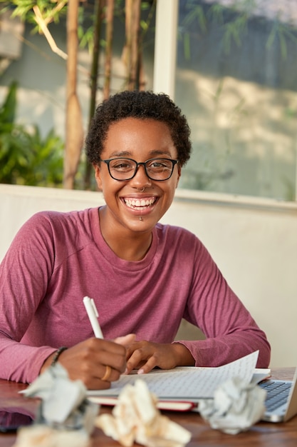 Cheerful smiling black college student works on course paper