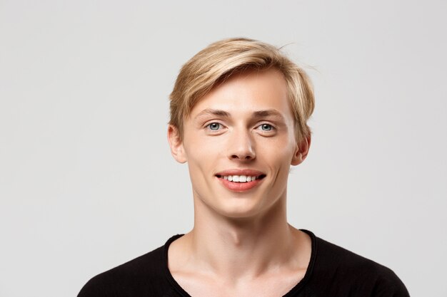  cheerful smiling blond handsome young man wearing black t-shirt on grey wall