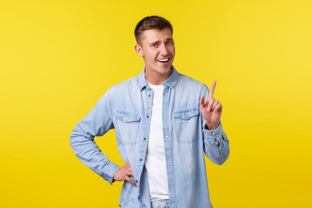 Cheerful smiling blond man shaking finger, tell not so fast, scolding someone or asking hold on, wait sec, standing yellow background upbeat, showing advertisement on top