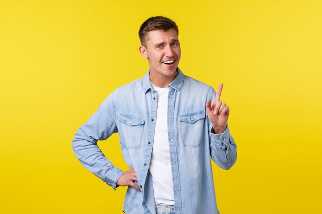 Cheerful smiling blond man shaking finger, tell not so fast, scolding someone or asking hold on, wait sec, standing yellow background upbeat, showing advertisement on top