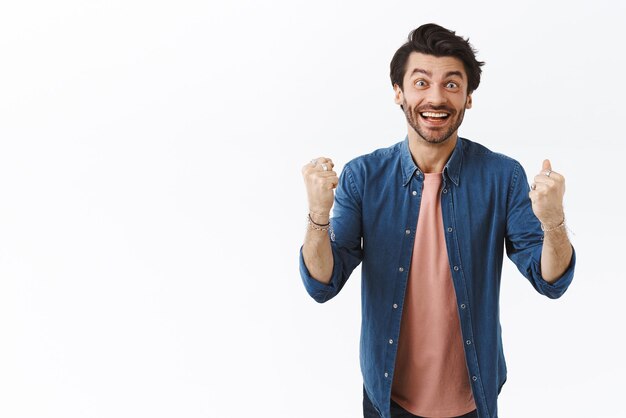 Cheerful smiling goodlooking guy rooting for team watching happily how player score goal clench fists and shaking arms in celebration triumphing fist pump smiling and stare camera excited