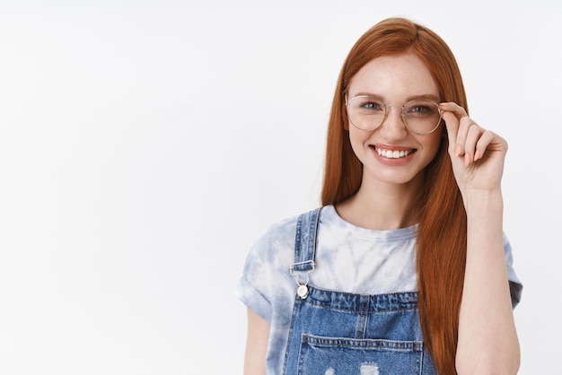 Cheerful smiling redhead young girl grinning confident checking transparent glasses on nose touch eyewear rim feeling selfassured motivated accomplish goal stand white background