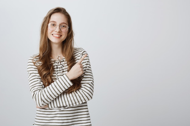 Cheerful smiling smart college girl in glasses pointing finger upper right corner