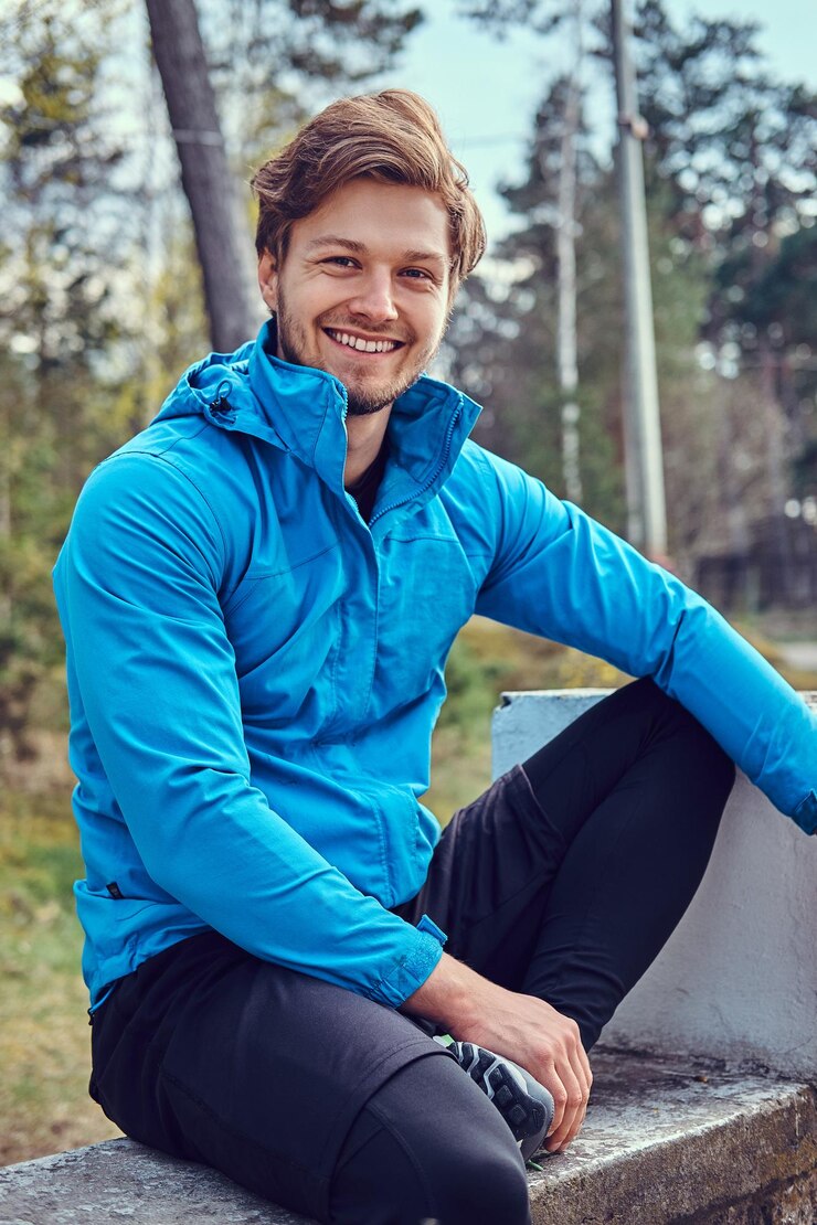 Free Photo cheerful smiling sportsman in activewear is relaxing on the bench at the park.