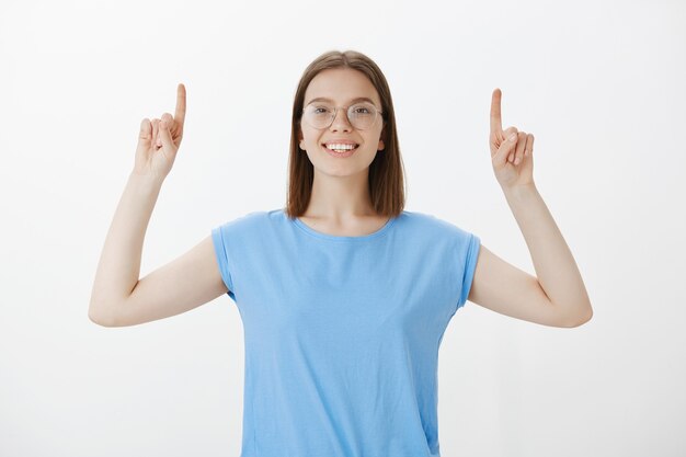 Cheerful smiling woman pointing fingers up and showing advertisement