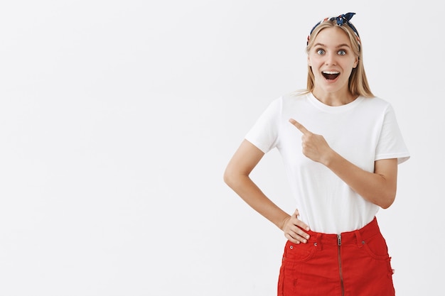 Giovane ragazza bionda sorridente allegra che posa contro il muro bianco