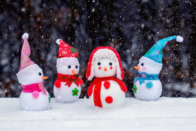 Веселые снеговики в лесу на темном фоне во время снегопада. рождественская и новогодняя открытка