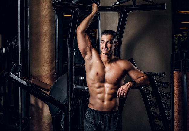 Cheerful sportive man is posing for photographer at dark gym club.