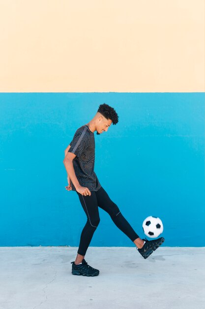 Веселый спортсмен пинает футбольный мяч у стены
