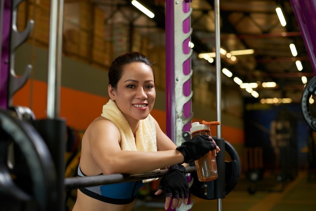 Cheerful sportswoman smiling at camera at the Smith machine in a gym